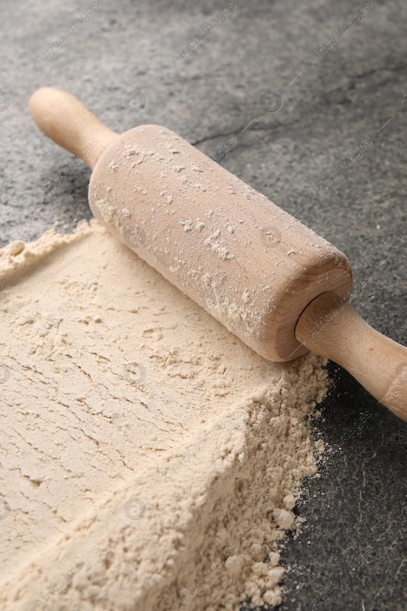 Photo of Scattered flour and rolling pin on grey textured table, closeup