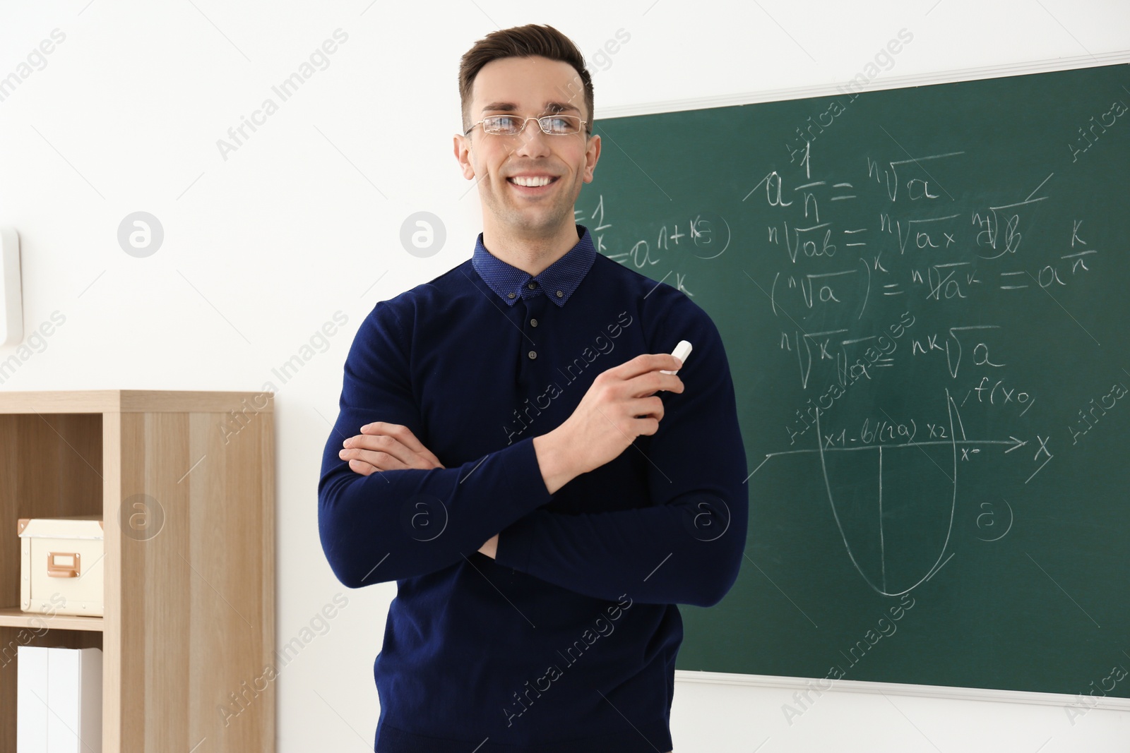 Photo of Young male teacher with chalk standing in classroom