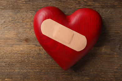 Photo of Heart with medical patch on wooden background, top view. Relationship problems concept