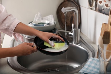 Photo of Woman washing dirty frying pan in sink indoors, closeup