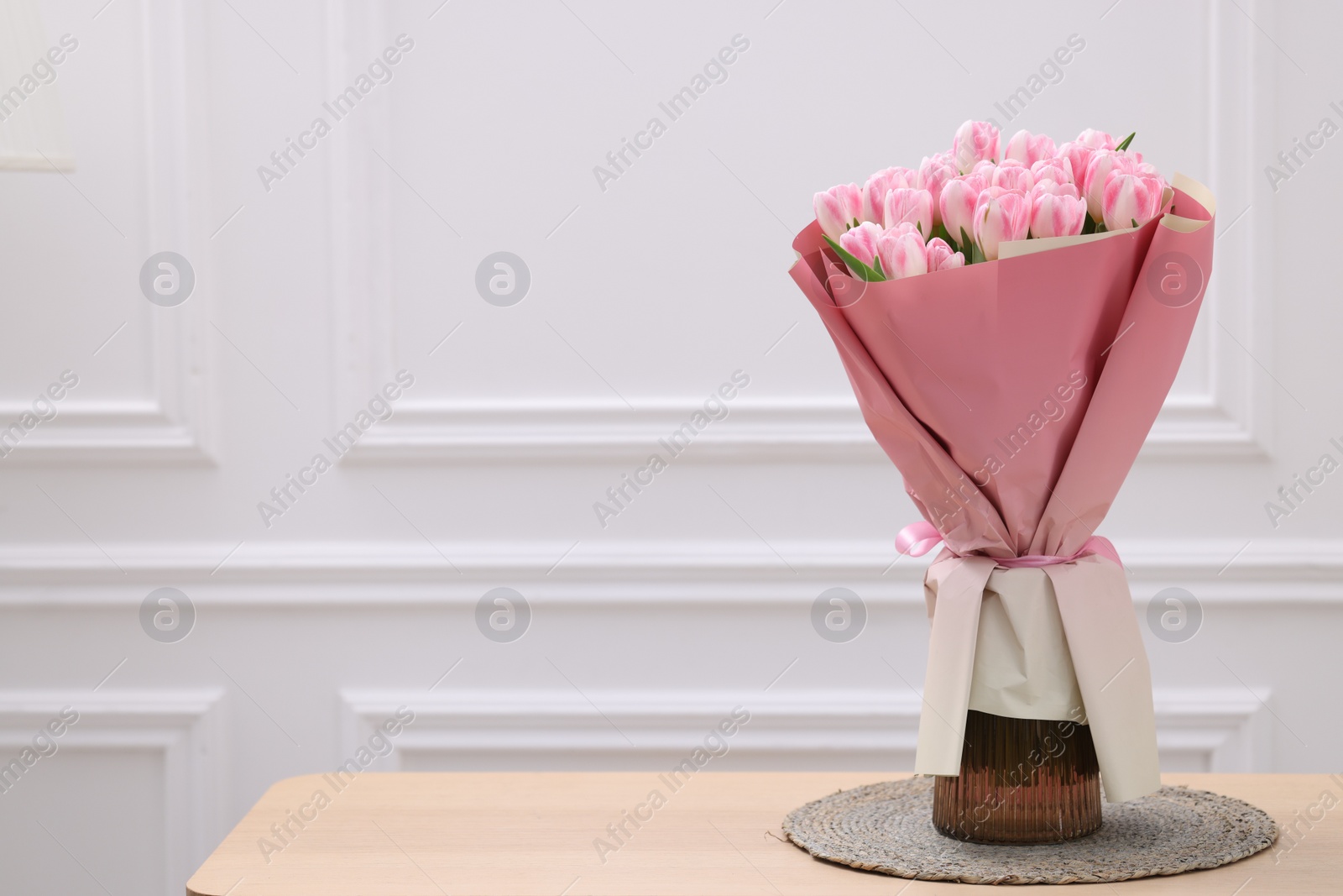 Photo of Beautiful bouquet of fresh pink tulips on wooden table near white wall. Space for text