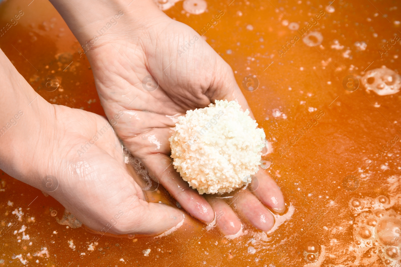 Photo of Woman holding bath bomb in orange water, closeup