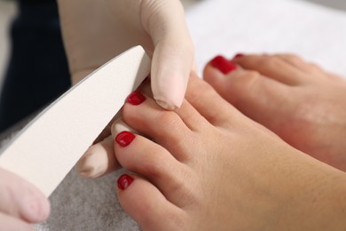 Photo of Pedicurist filing client`s toenails in beauty salon, closeup