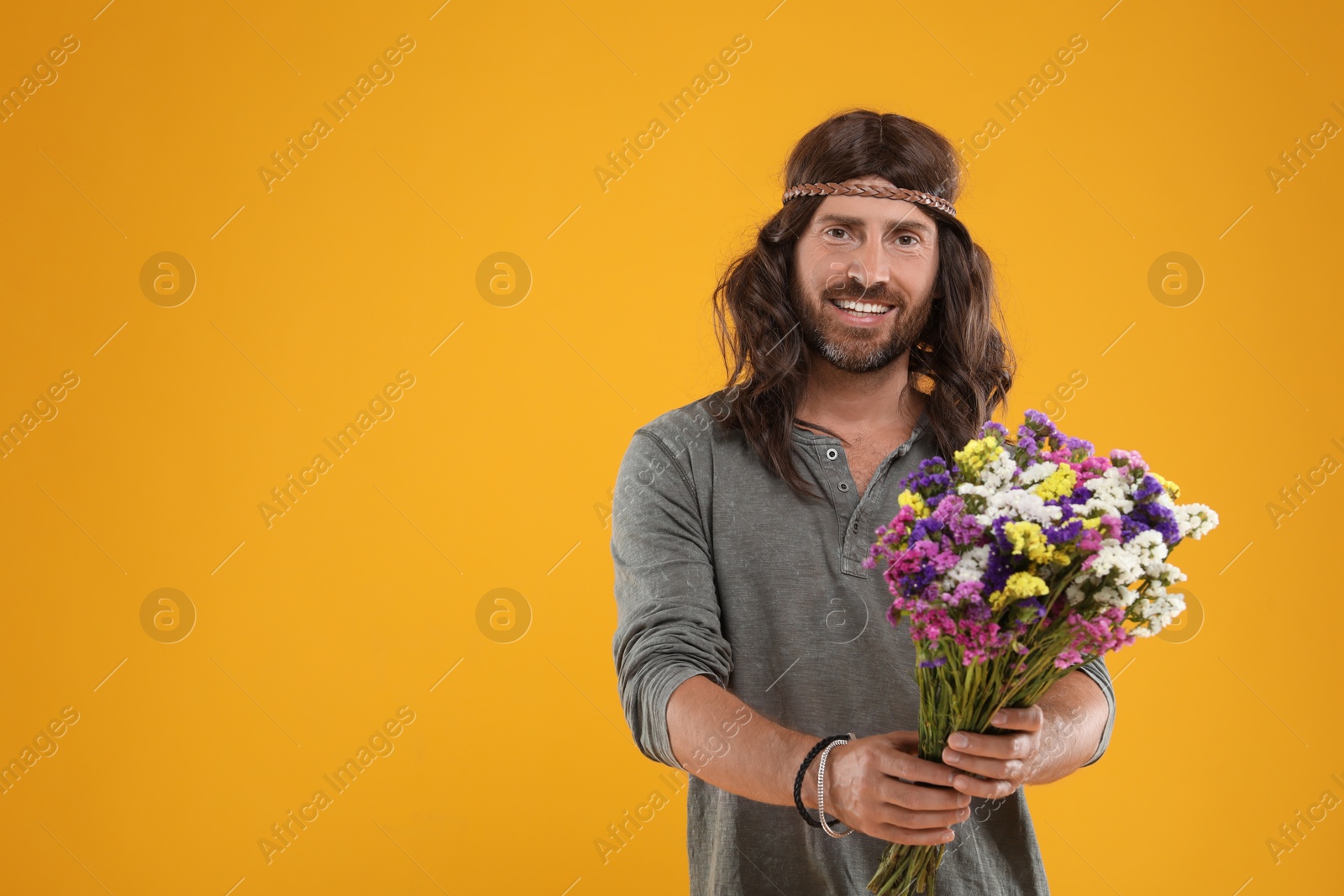 Photo of Hippie man with bouquet of colorful flowers on orange background, space for text