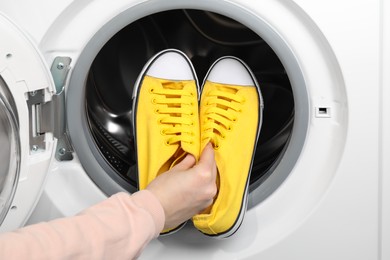 Photo of Woman putting stylish sneakers into washing machine, closeup