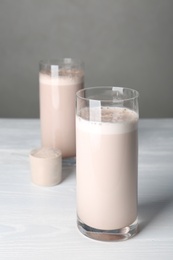 Glasses with protein shake and scoop of powder on white wooden table