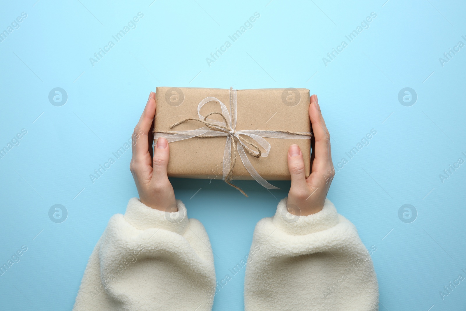 Photo of Woman holding Christmas gift box on light blue background, top view