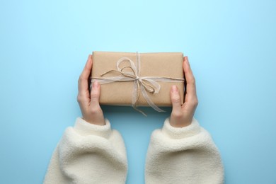 Woman holding Christmas gift box on light blue background, top view