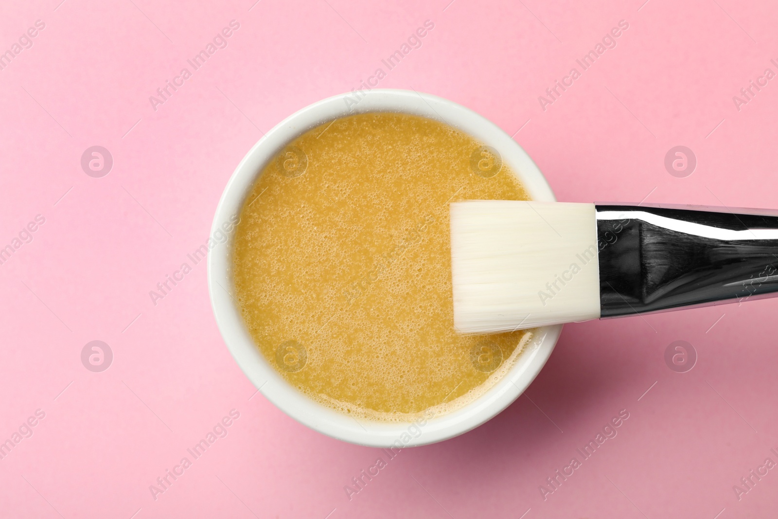 Photo of Bowl with handmade face mask and brush on pink background, top view