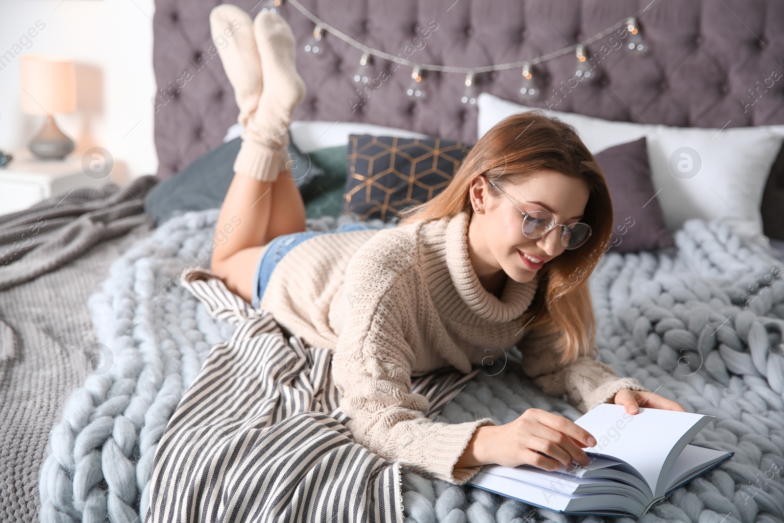 Photo of Young woman reading book on bed at home