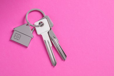 Keys with keychain in shape of house on pink background, top view. Space for text