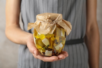 Woman holding jar with pickled feta cheese on beige background, closeup