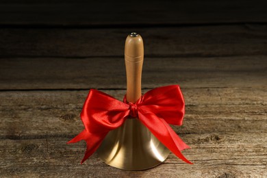 Photo of Golden bell with red bow on wooden table. School days