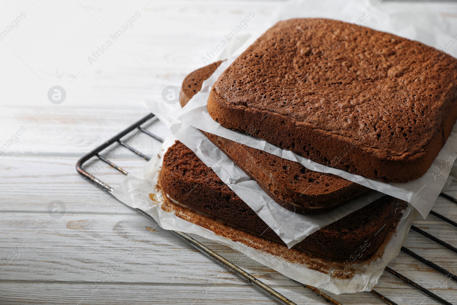 Photo of Layers of homemade chocolate sponge cake on white wooden table, closeup. Space for text