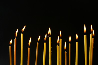 Many burning church candles on black background