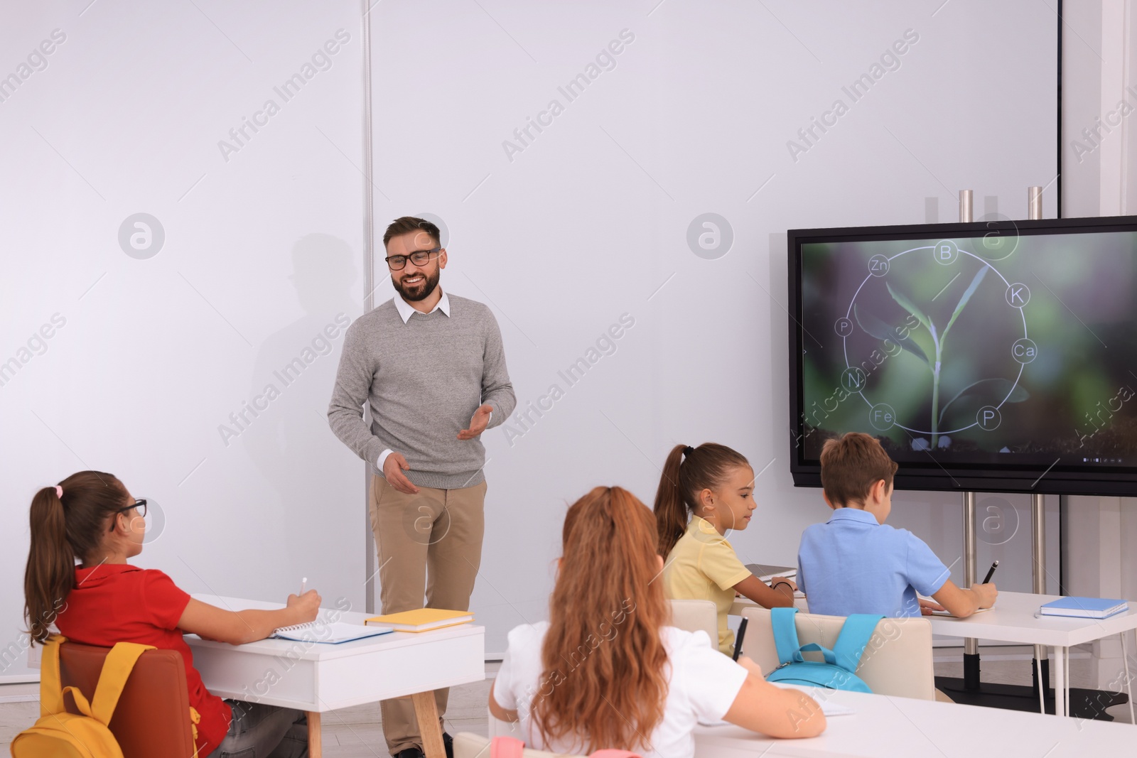 Photo of Teacher giving lesson to pupils near interactive board in classroom