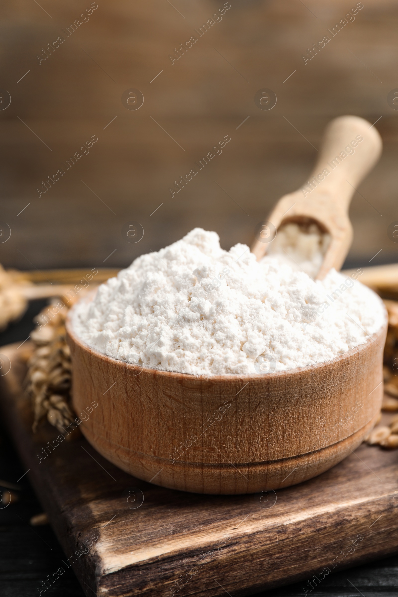 Photo of Wheat flour in bowl, spike and grains on black table, closeup