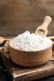 Wheat flour in bowl, spike and grains on black table, closeup