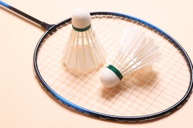 Feather badminton shuttlecocks and racket on beige background, closeup