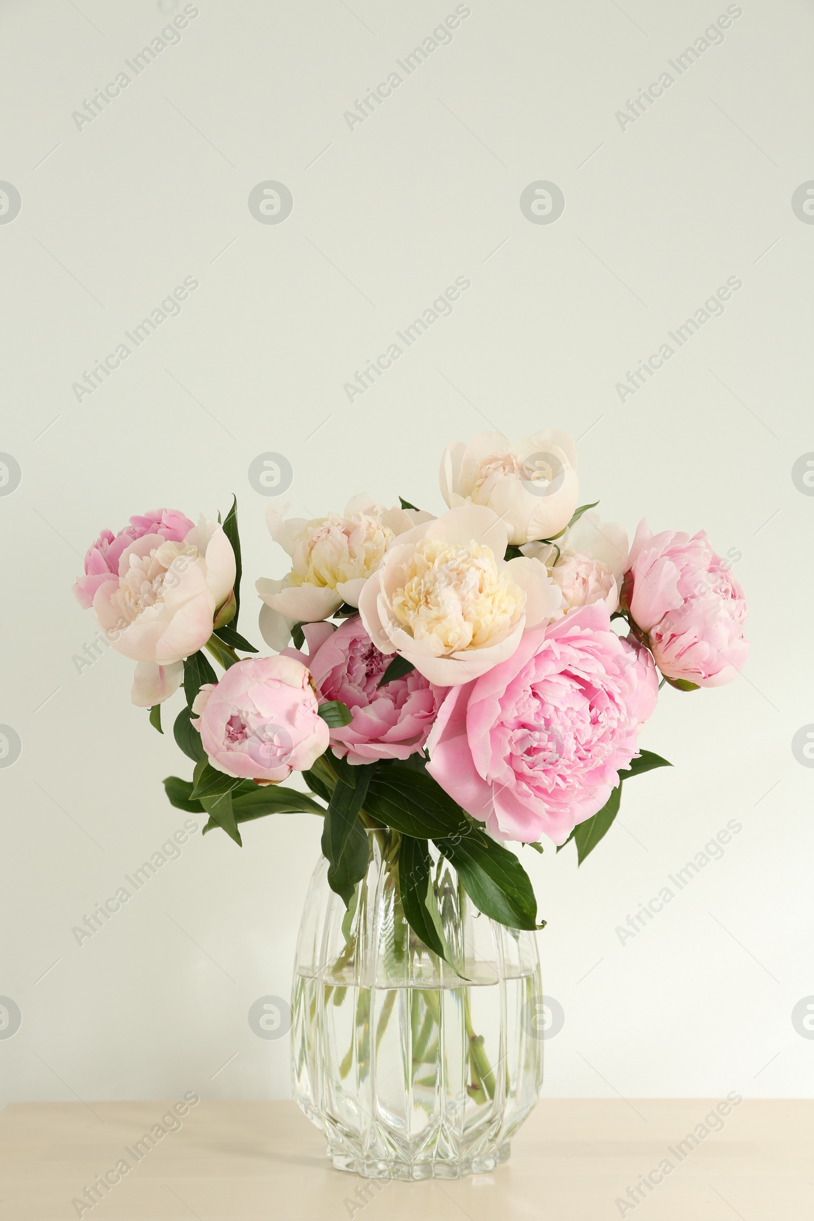 Photo of Bouquet of beautiful peonies in glass vase on beige table