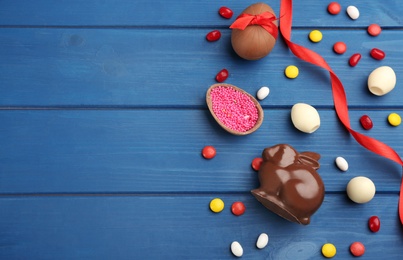 Photo of Chocolate Easter bunny, candies and eggs on blue wooden table, flat lay. Space for text