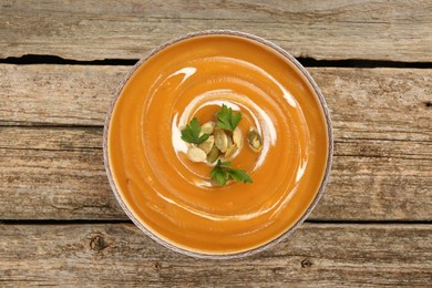 Photo of Delicious pumpkin soup with seeds and parsley in bowl on wooden table, top view