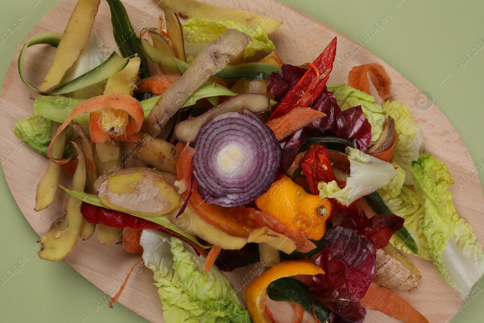 Photo of Peels of fresh vegetables with wooden board on light green background, top view