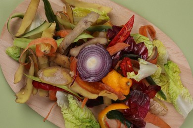 Peels of fresh vegetables with wooden board on light green background, top view