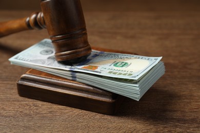 Law gavel with stack of dollars on wooden table, closeup