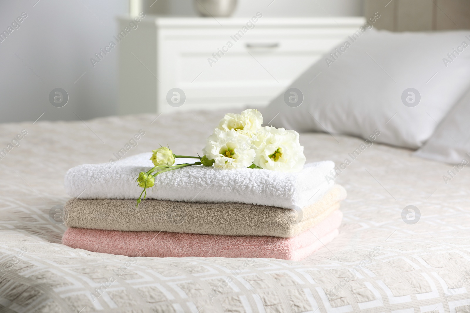 Photo of Terry towels with beautiful flowers on bed indoors, space for text