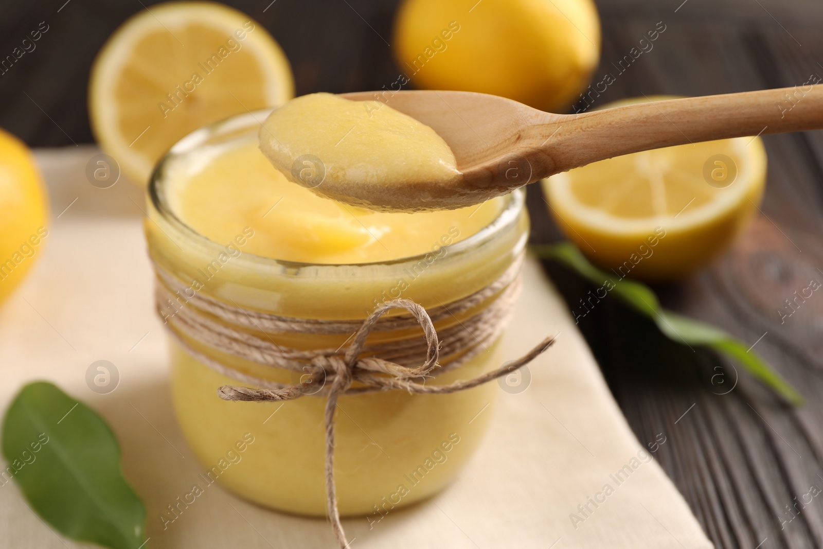 Photo of Taking delicious lemon curd from glass jar at wooden table, closeup