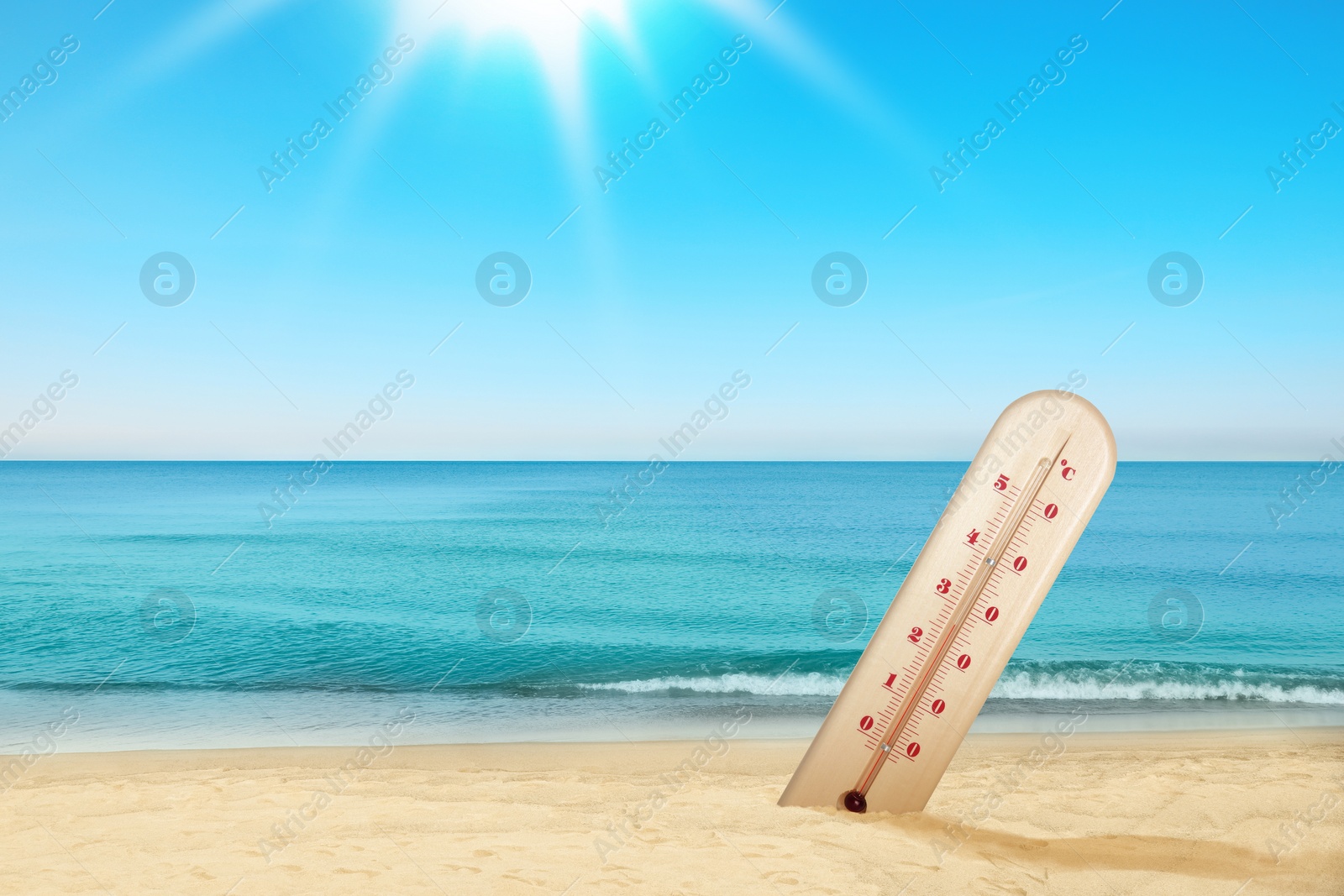 Image of Thermometer in sand on beach during sunny summer day