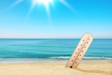 Image of Thermometer in sand on beach during sunny summer day