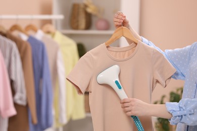 Woman steaming shirt on hanger at home, closeup. Space for text