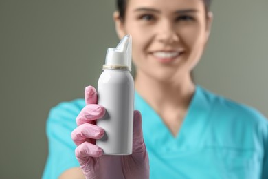 Woman holding nasal spray bottle on olive background, selective focus