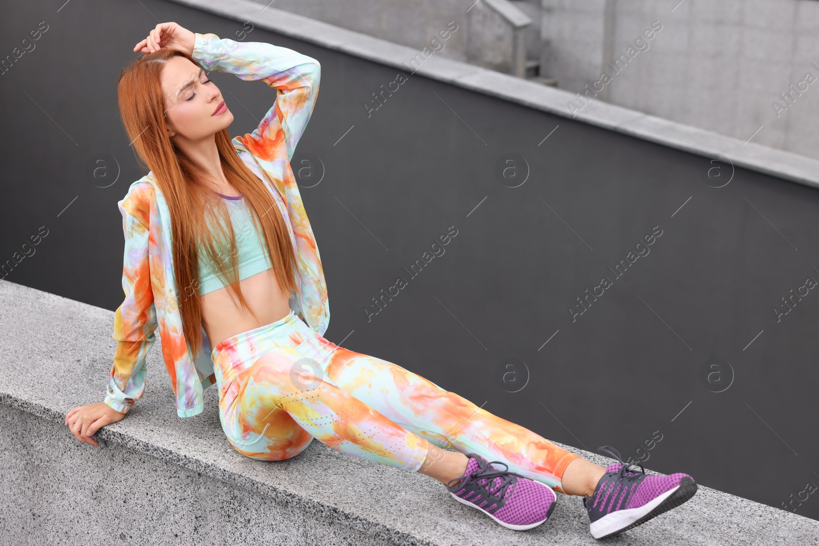 Photo of Beautiful woman in gym clothes sitting on parapet on street