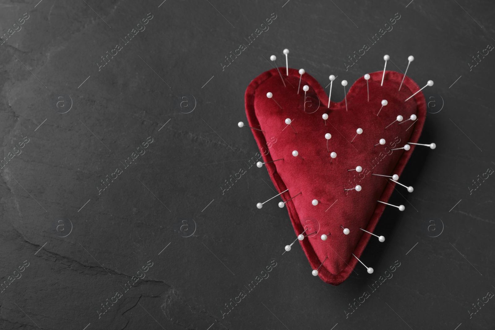 Photo of Top view of heart shaped cushion with sewing pins on black stone background, space for text. Relationship problems concept