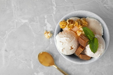 Photo of Bowl of delicious ice cream with caramel candies, popcorn and mint on light grey marble table, flat lay. Space for text