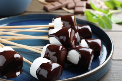 Delicious marshmallows covered with chocolate on plate, closeup