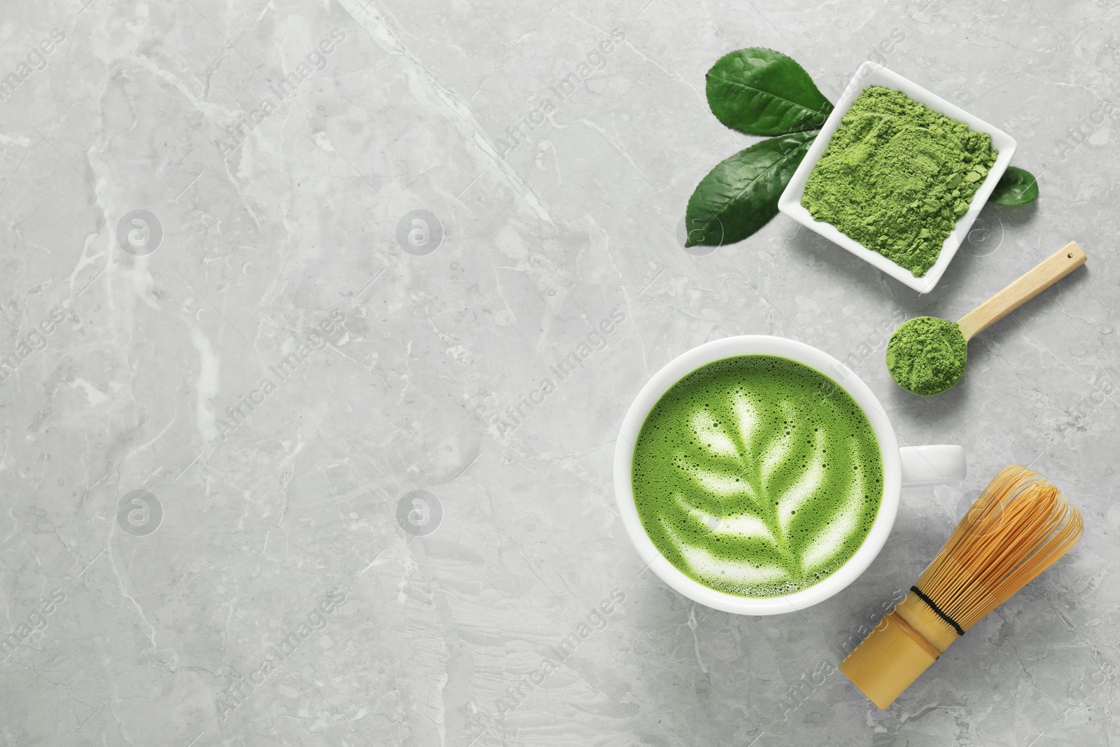 Photo of Cup of fresh matcha latte, powder and bamboo whisk on grey marble table, flat lay. Space for text
