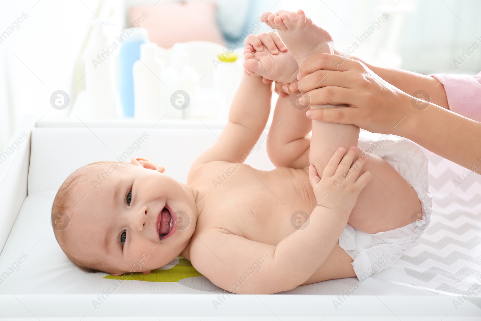 Photo of Young woman massaging cute baby on changing table