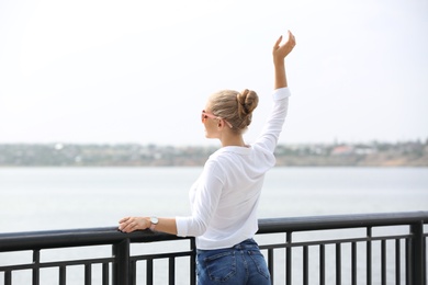 Beautiful young woman with sunglasses standing at pier. Joy in moment