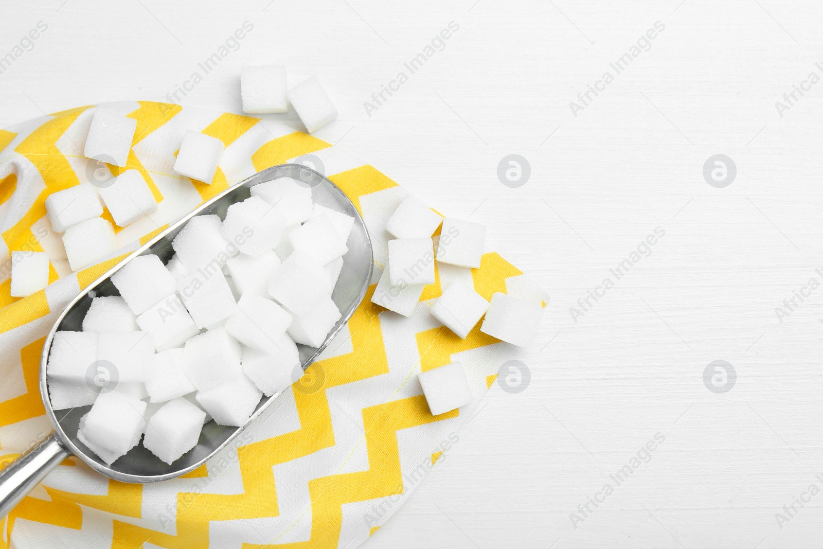 Photo of Many sugar cubes and metal scoop on white wooden table, top view. Space for text