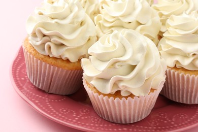 Photo of Tasty vanilla cupcakes with cream on pink table, closeup