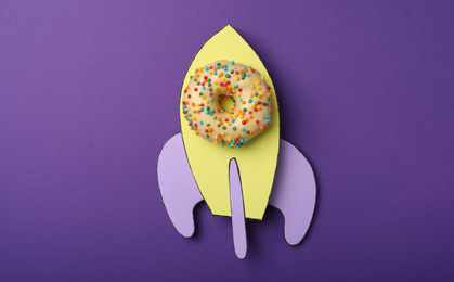 Photo of Rocket made with donut and paper on purple background, top view