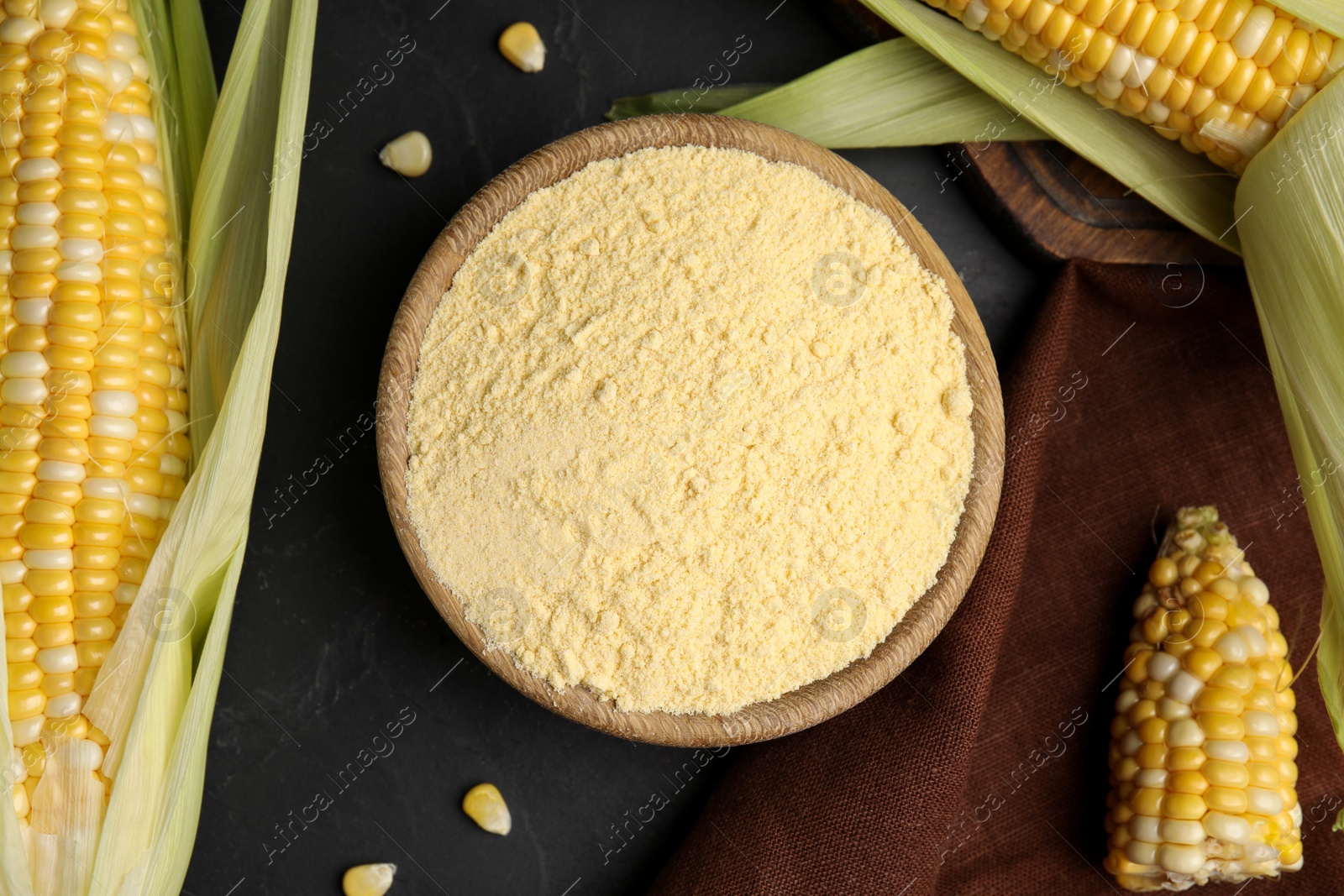 Photo of Corn flour in bowl and fresh cobs on black table, flat lay