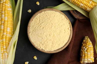 Photo of Corn flour in bowl and fresh cobs on black table, flat lay