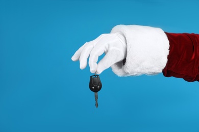 Photo of Santa Claus holding car key on blue background, closeup of hand