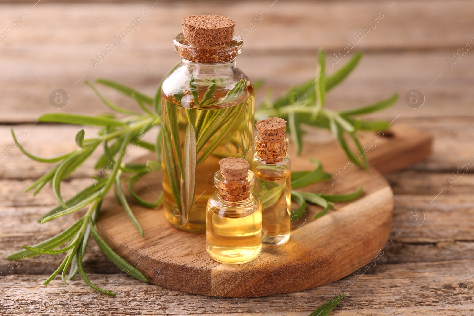 Photo of Aromatic essential oils in bottles and rosemary on wooden table, closeup