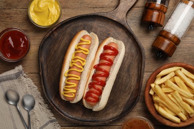 Delicious hot dogs with mustard, ketchup and potato fries on wooden table, flat lay